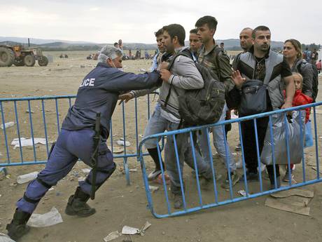 A policeman pushes refugees behind a barrier at Greece's border with Macedonia, near the village of Idomeni